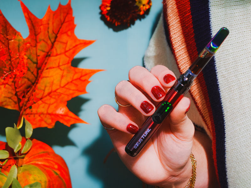 woman with red nails holding Exxus Tunl with fall leaves and blue background